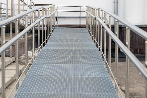 Metal ramp with railing for sedentary people. The path is up with a right turn. Front view.