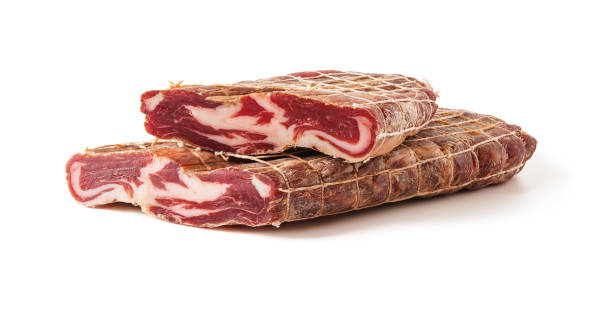 tagliare a metà pezzo di gustoso cured meat da vicino. ruolo trapezitsa tradizionale prelibatezza di carne bulgara di collari di maiale crudi pressati con sale, aglio e pepe isolati su sfondo bianco. - dry cured ham foto e immagini stock