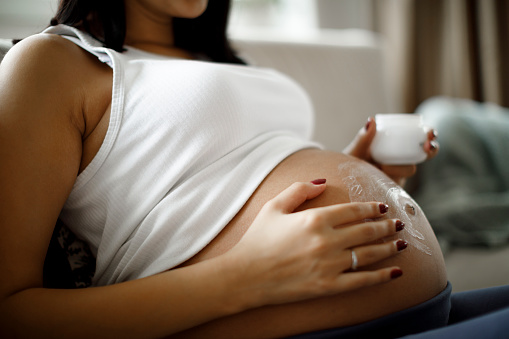 Mujer embarazada aplicando crema para el cuidado de la piel en su vientre para evitar la estrías photo