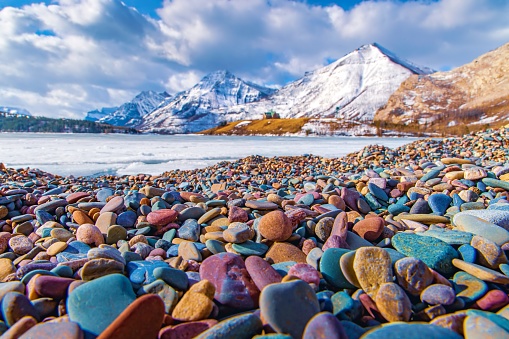 A view of the colourful rocks at Driftwood beach from across a frozen Waterton Lakes in the winter.