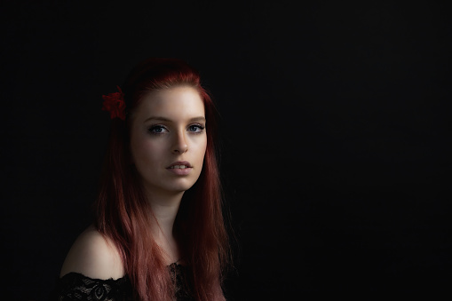 Low key portrait of beautiful young woman with red rose in her red hair. Horizontally.