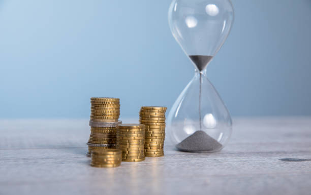 istock Hourglass with coins on gray background 1309629168