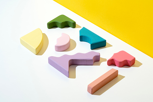 Colorful wooden stacking toy, puzzle, toy blocks. Pastel colored geometric wooden shapes flat lay on yellow and white background.