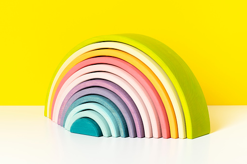 Colorful, arched building blocks. Pastel colored wooden rainbow stacker toy on yellow background.