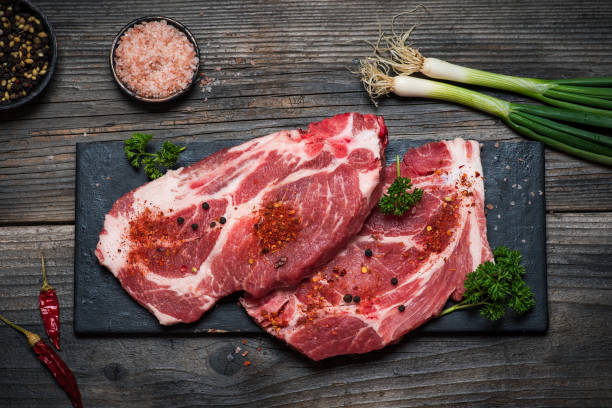 Fresh raw pork neck steak with bone with spices and cooking ingredients ready for cooking. Fresh pork meat on rustic wooden table