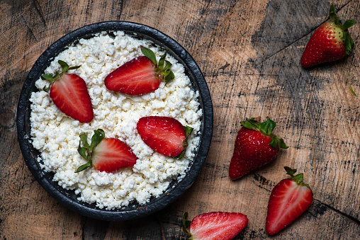 Cottage cheese, crumbled cheese with fresh strawberries in a bowl, table top view. Healthy dairy product rich in Calcium and Protein with vitamin filled berry fruits. Homemade soft white cheese