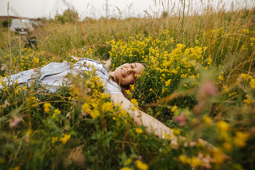 Beautiful carefree young woman with a dental prosthesis and wildflowers in top jeans pocket lying on back and relaxing in a field of grass and wildflowers on sunny spring day