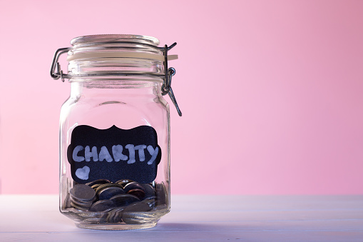 Glass jar with coins with chalk tag Charity on a pink background, donation and charity concept. Copy space.