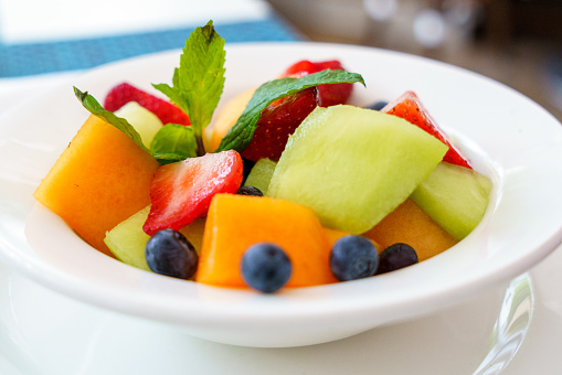 A bowl of fresh fruit including strawberries, cantaloupe, melon and blueberries.