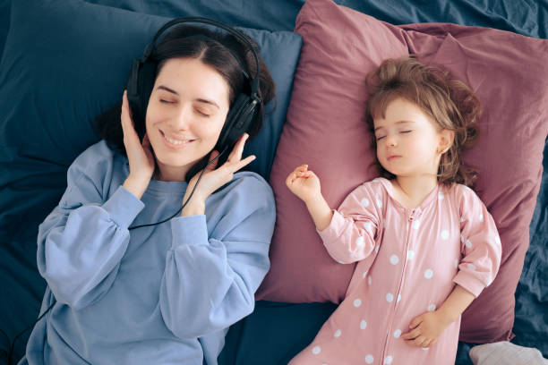 madre usando auriculares escuchando un podcast mientras el bebé duerme - mothers audio fotografías e imágenes de stock