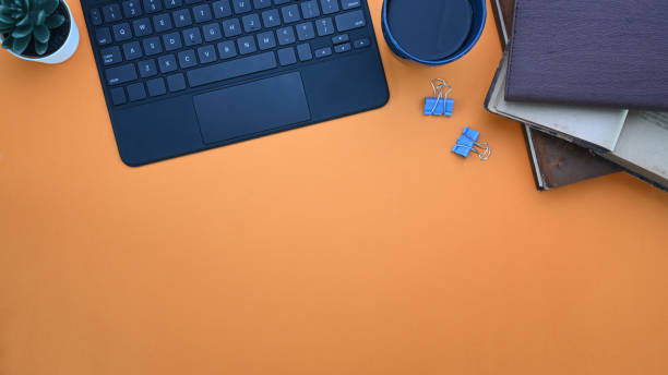 istock Stylish workplace with notebook ,coffee cup, keyboard and copy space on orange background. 1309686185