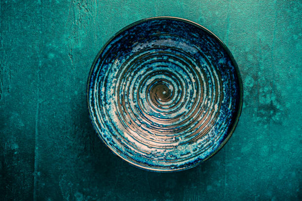 Close-up of a handmade ceramic bowl with blue marble pattern placed on a textured dark wooden surface. Ideal for craft design, kitchenware promotion, or minimal food styling.