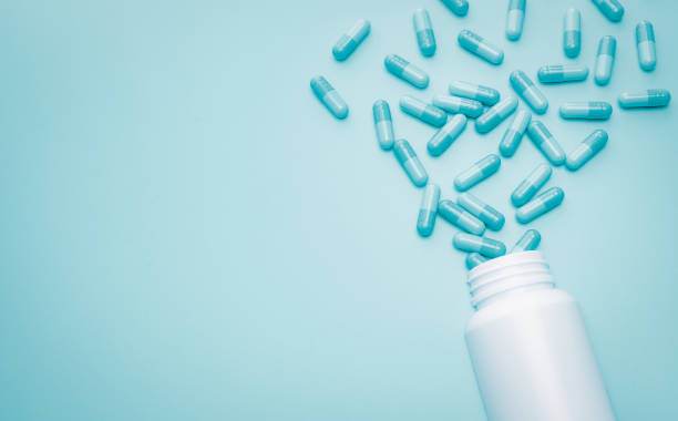 Blue capsule pills spread out of white plastic drug bottle on blue background. Pharmacy web banner. Antibiotic drug resistance or superbug concept. Health budget and policy. Antibiotic drug overuse. píldoras cápsula azules se propagan fuera de la botella de drogas de plástico blanco sobre fondo azul. banner web de farmacia. resistencia a los antibióticos o concepto de superbug. presupuesto y política de salud. uso excesivo de antibióticos.
