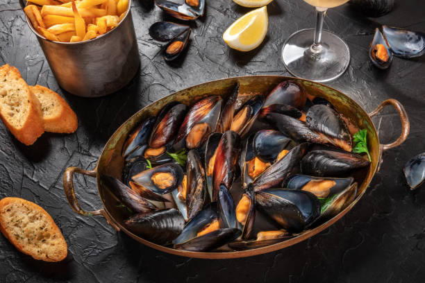 Moules frites, mussels with fries, with lemon and toasts Moules frites, mussels with fries, with lemon and toasts on a dark background moules frites stock pictures, royalty-free photos & images