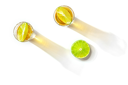 Tequila shots with salty rims and lime slices, overhead flat lay shot on a white background
