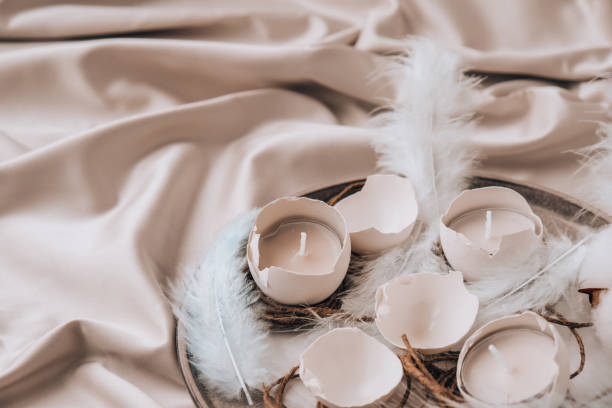 istock Trendy Easter decorations. Cracked organic eggs on plate. Candle in White shell of the eggs. Bird feather. Copy space. Greeting card. Pastel colors 1309692335