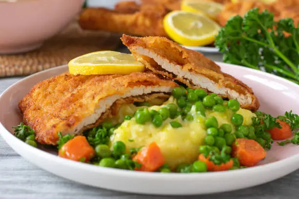 Traditional german Schnitzel with mashed potatoes and buttered peas and carrots served with lemon slices on a plate for dinner