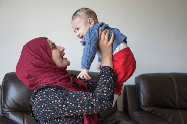 Candid portrait of British Asian mother with happy baby boy Side view of mid adult woman in headscarf and tunic face to face with her laughing 5 month old son as they enjoy time together in living room of family home. candid bonding connection togetherness stock pictures, royalty-free photos & images