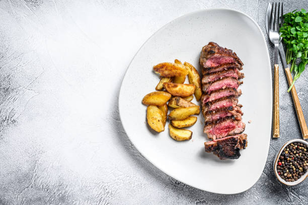 istock Sliced striploin steak with potato. White background. Top view. Copy space 1309696664