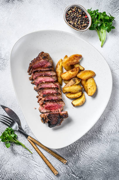 istock Sliced striploin steak with potato. White background. Top view 1309697216