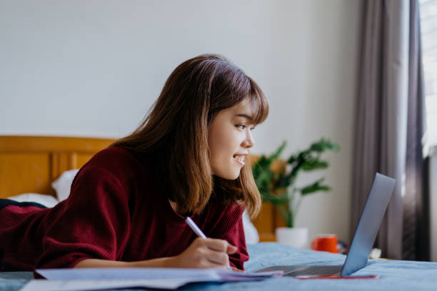 istock Young asian woman writing on paper and using laptop on bed 1309697496