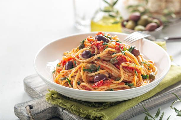 Italian lunch. Spaghetti alla puttanesca - italian pasta dish with tomatoes, olives, capers and parsley. Light background. Copy space. stock photo