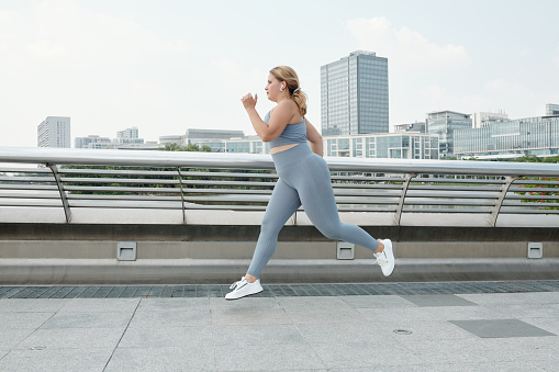 Fit plus size young woman listening to music when running outdoors and training for marathon
