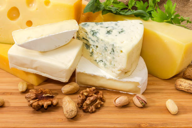istock Different types cheese among greens and nuts on wooden surface 1309699993