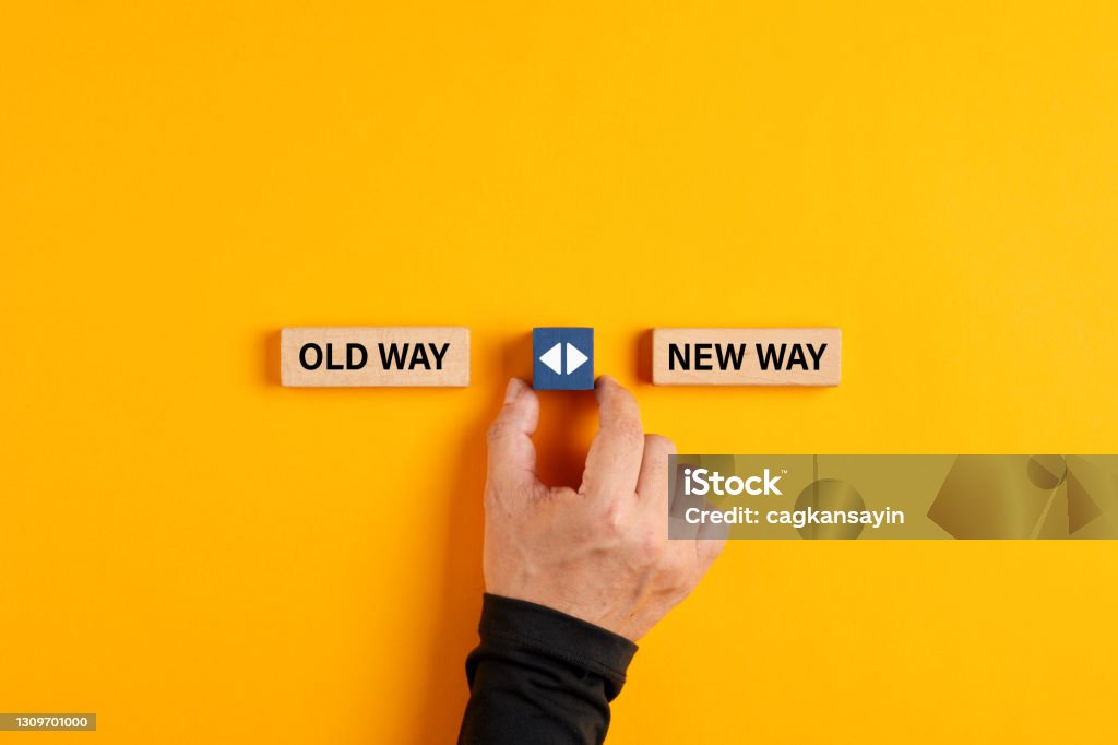 Male hand holds a wooden cube with arrow icon between the options of old way or new way. Male hand holds a wooden cube with arrow icon between the options of old way or new way. Deciding to do things in a traditional or a modern fashionable way Change Stock Photo