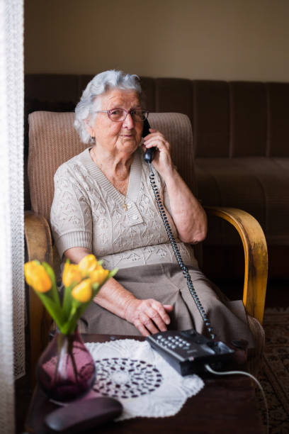 istock Cute old lady sitting at sofa and having phone conversation 1309701137