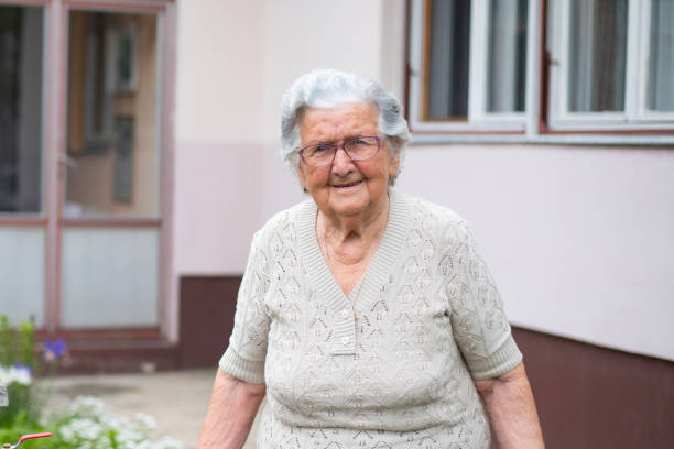 Smiling pleasant 80s elderly mother looking at camera, posing for photo in modern living room.