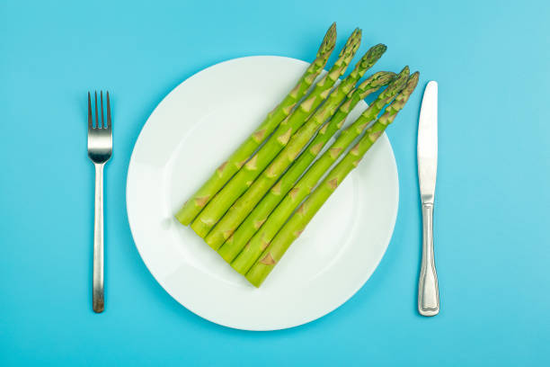 Asparagus on a white plate on a blue background. Fresh vegetable asparagus for a healthy diet and nutrition. Vegetables and healthy food concept Asparagus on a white plate on a blue background. Fresh vegetable asparagus for a healthy diet and nutrition. Vegetables and healthy food concept. High quality photo asparagus organic dinner close to stock pictures, royalty-free photos & images