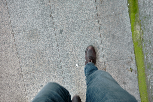 A man foot boots walking on paving floor made of stone material in pedestrians way tiles in istanbul. Man wearing blue jean.