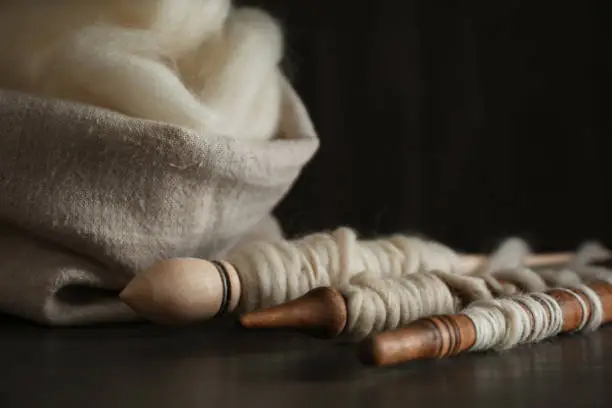 Soft white wool and spindles on wooden table, closeup