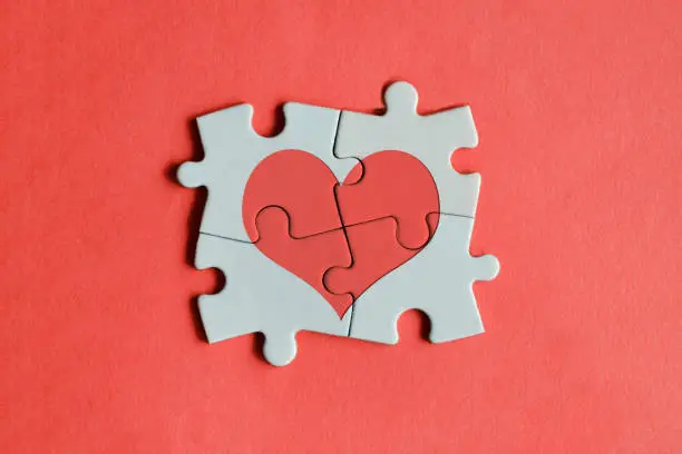 Red heart shape on the jigsaw puzzle pieces. Red background with horizontal composition.