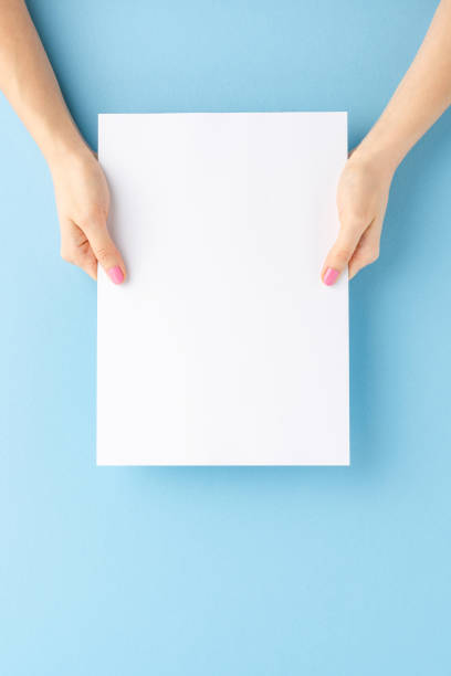 istock Young woman’s hands holding blank paper sheet on blue background. Mockup 1309708037