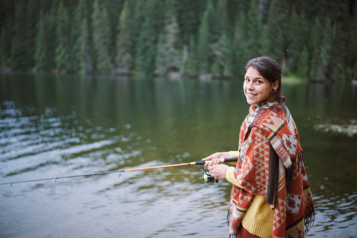 Shot of a beautiful woman holding fishing rod, smiling and looking at the camera.