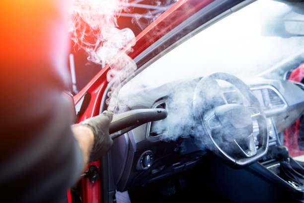istock Car service worker cleans interiror with steam cleaner 1309713321