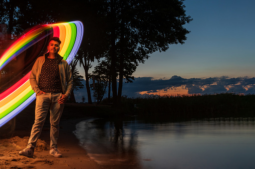 young man standing on a calm lake sand shore with rainbow abstract light behind him