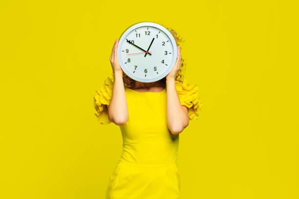 istock beautiful young woman  posing  on yellow  background with clocks  - Image 1309716246