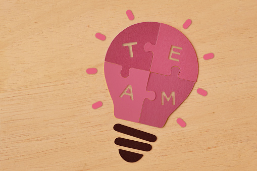 Pink paper light bulb made of puzzle pieces with the word Team - Concept of women and teamwork