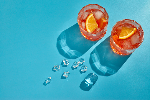 Cocktail. Two glasses with cool beverages, sliced oranges and ice on blue background with shadow. Top view with copy space