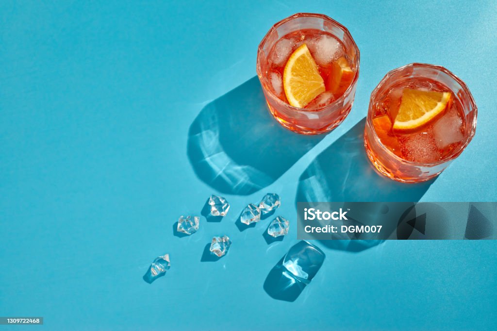 Cocktail. Two glasses with cool beverages, sliced oranges and ice on blue background with shadow. Top view with copy space Cocktail. Fresh orange juice. Two glasses with cool beverages, sliced oranges and ice on blue background with shadow. Top view with copy space Cocktail Stock Photo