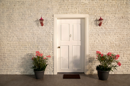 La puerta de la casa y las flores frente a la puerta. Pared de piedra blanca, flores rosadas y árboles photo