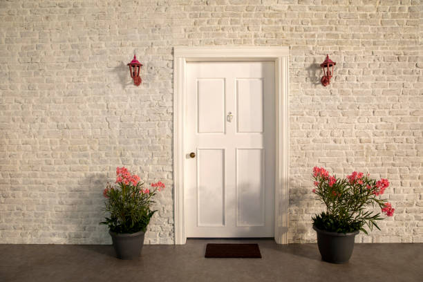 The door of the house and the flowers in front of the door. White stone wall, pink flowers and trees The door of the house and the flowers in front of the door. White stone wall, white door, pink flowers, plants, black flowerpots and trees pink flowering dogwood stock pictures, royalty-free photos & images