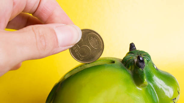 Hand throws coin into piggy bank on yellow background