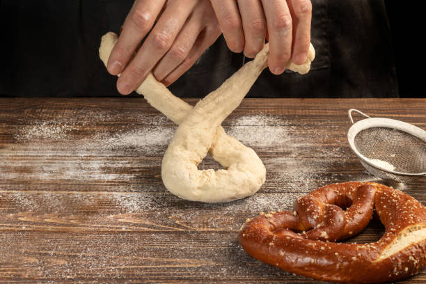 step-by-step instructions for making pretzels. the cook rolls out the dough and rolls out the pretzel. dark background. - dough sphere kneading bread imagens e fotografias de stock