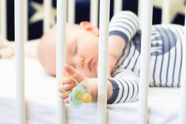 istock Little baby boy peacefully sleeping in the bed holding pacifier dummy in his hand 1309742855