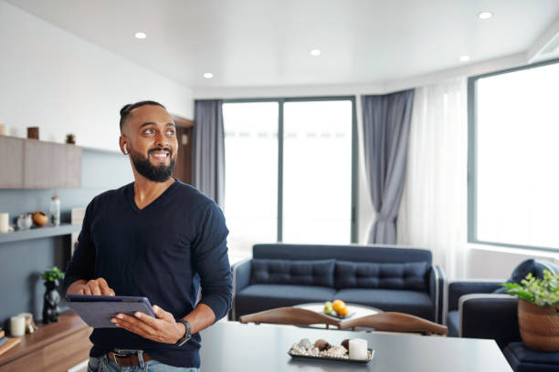 Cheerful man with digital tablet Portrait of happy excited bearded man using smart home application on digital tablet to open curtains and turn off light in his apartment home automation stock pictures, royalty-free photos & images