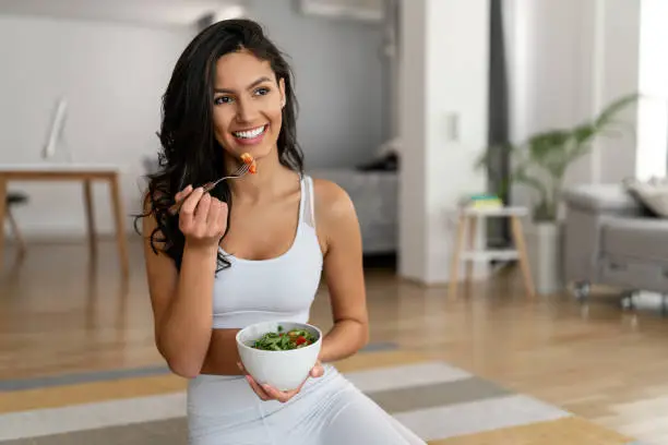 Photo of Young woman eating a healthy salad after workout. Fitness and healthy lifestyle concept.